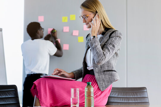 Businesswoman talking on smart phone while male colleague working in background at office