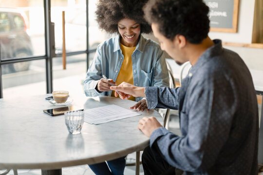 Male customer and businesswoman signing contract while sitting in cafe