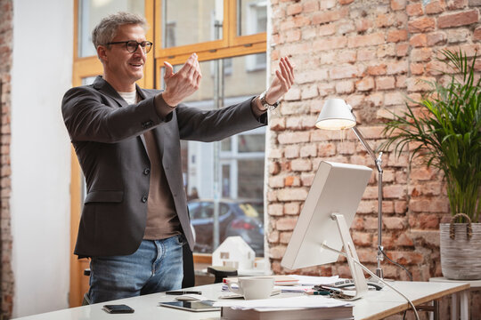 Mature businessman gesturing while standing by desk at work place