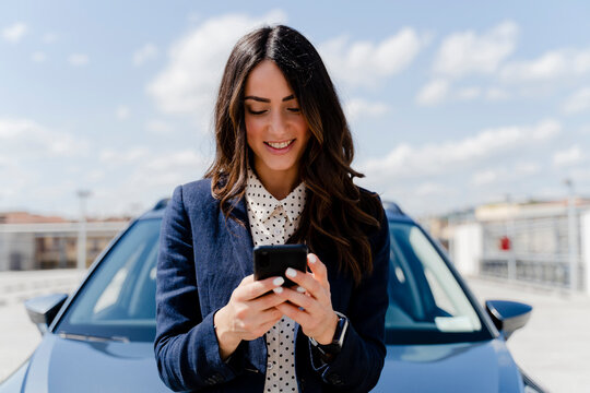 Smiling businesswoman using smart phone by car