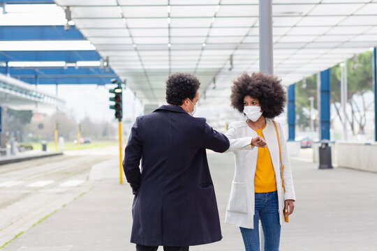 Woman with protective face mask giving elbow bump to male friend at railroad station