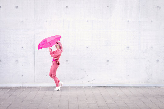 Happy woman holding pink umbrella on footpath