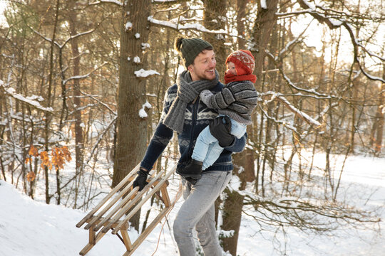 Father with sled holding son while walking in snow during winter