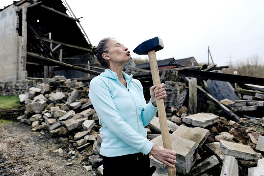 Woman puckering while holding hammer with demolished house in background