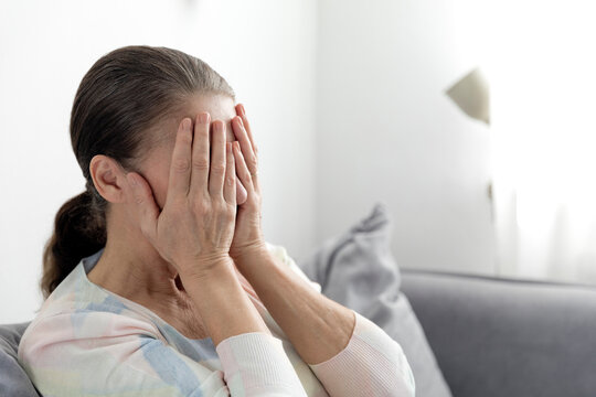 Worried woman covering face with hands at home