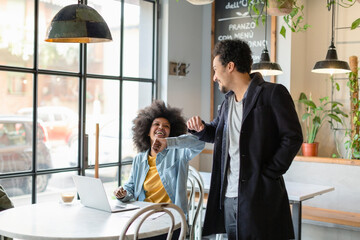 Smiling female entrepreneur giving elbow bump to male coworker in cafe