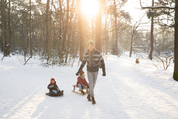 Father pulling sons sitting on sled in snow during sunny day