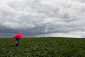 Woman with red umbrella standing in grass during stormy weather