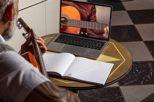 Man playing acoustic guitar and watching online classes on laptop while practicing at home..Online training, online classes.