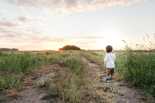 Baby boy standing in middle of countryside dirt road at sunset