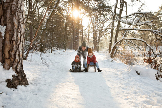 Father pushing sons sitting on sled during winter