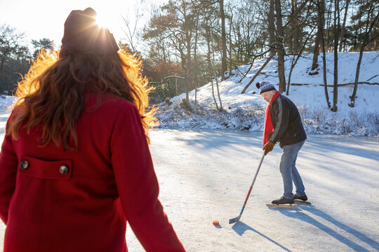 Senior man playing ice hockey with woman on snow during winter