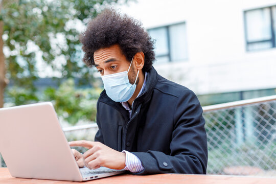 Afro businessman wearing face mask working on laptop during COVID-19