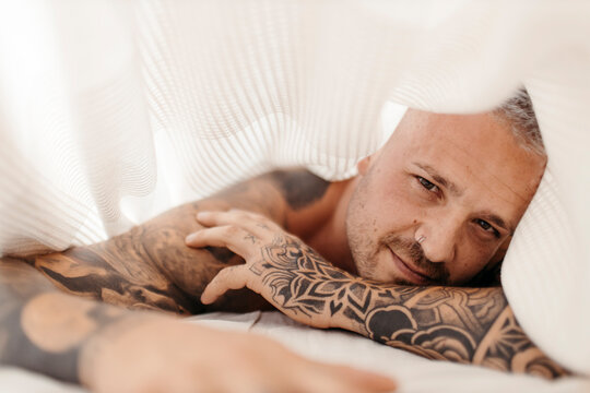 Hipster man lying on bed under blanket at home