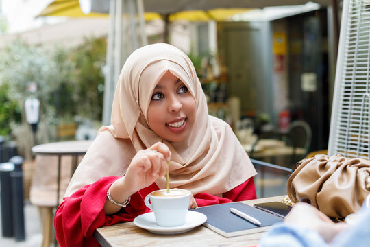 Smiling young woman stirring coffee while sitting at sidewalk cafe