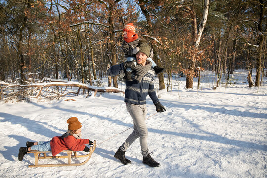 Father carrying son on shoulder while pulling sled on snow during winter