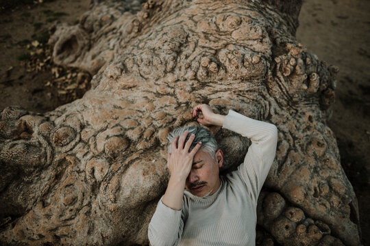Mature man with hand on forehead lying on tree roots