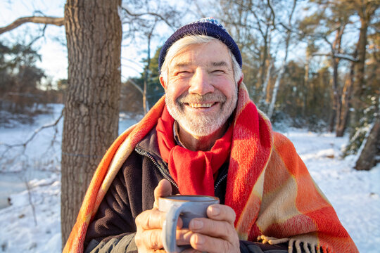 Smiling senior man in blanket holding coffee cup during winter