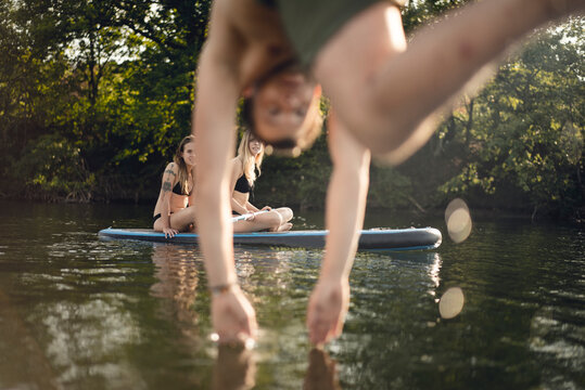 Young man diving into lake, young women on paddleboard warching