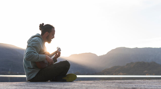 Young man singing while playing ukulele on promenade during sunny day