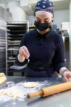 Female baker sprinkling flour while rolling dough at bakery