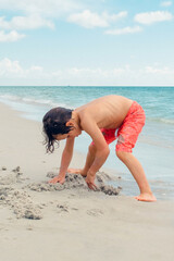 Child play on a tropical beach. Kid playing in the sea on summer family vacation. Children have fun at the beach resort. Funny boy writes on the sand.Active children's lifestyle, swimming people