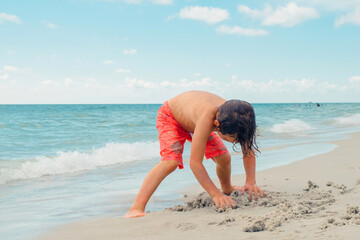 Child play on a tropical beach. Kid playing in the sea on summer family vacation. Children have fun at the beach resort. Funny boy writes on the sand.Active children's lifestyle, swimming people