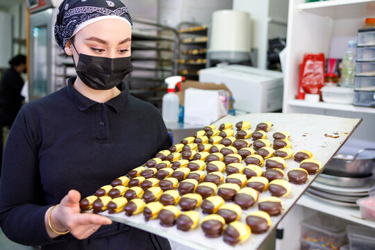 Female owner wearing protective face mask holding tray at bakery