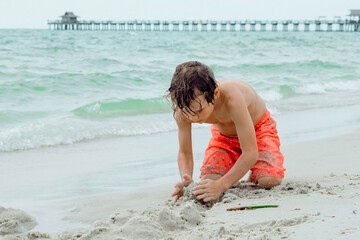 Child play on a tropical beach. Kid playing in the sea on summer family vacation. Children have fun at the beach resort. Funny boy writes on the sand.Active children's lifestyle, swimming people