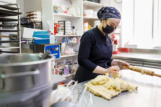 Female baker with rolling pin and dough in commercial kitchen at bakery