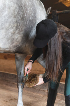 Woman cleaning horse hoof with brush in stable