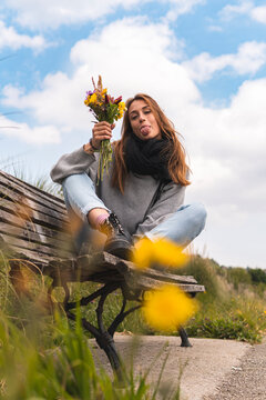 Young woman sticking out tongue while sitting with bunch of flowers on bench