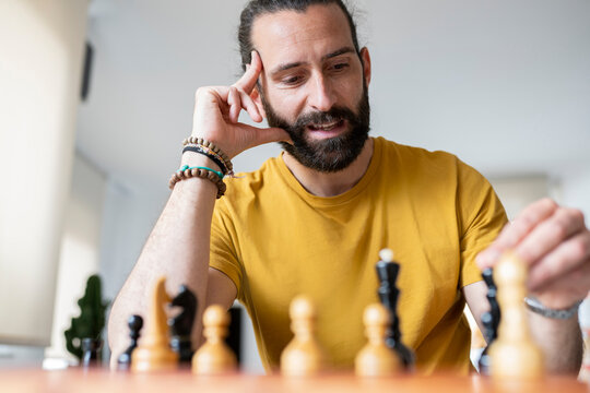 Man with head in hand playing chess at home