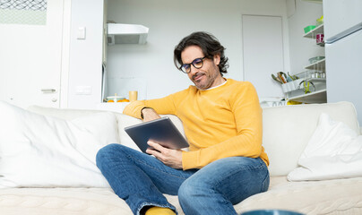 Man with eyeglasses using digital tablet while sitting on sofa in living room