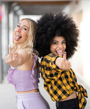 Multi-ethnic female friends sticking out tongue while showing middle finger