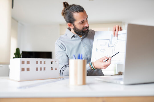 Male architect explaining construction plan over video call on laptop at home