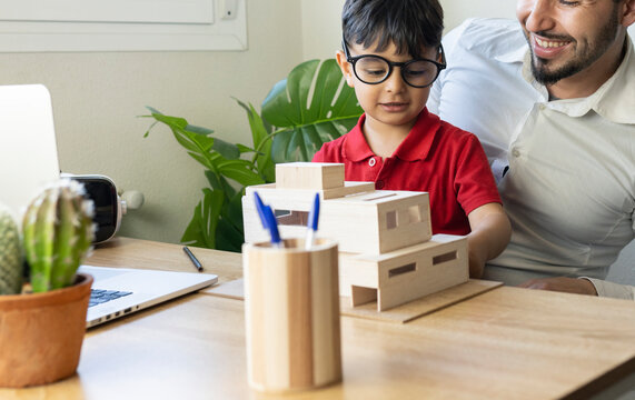 Boy with eyeglasses looking at house model while sitting with father at home
