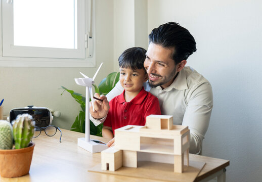 Smiling male architect showing turbine model to son at home office
