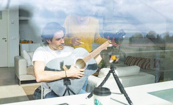 Woman discussing with man holding guitar while vlogging at home