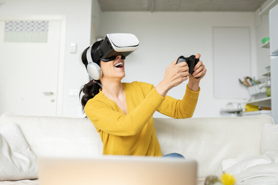 Laughing woman playing game wearing Virtual reality headset at home
