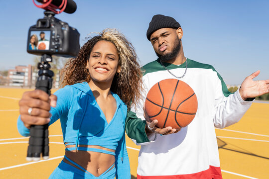 Female and male with basketball vlogging on sports court