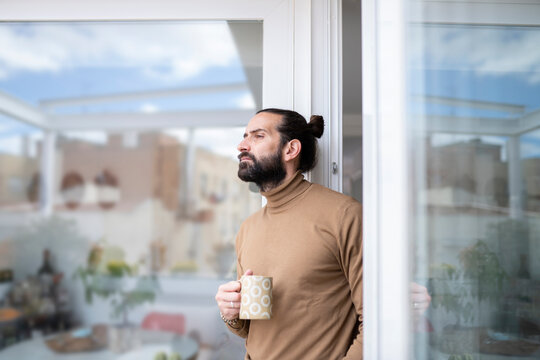 Thoughtful man with mug looking away while standing at doorway