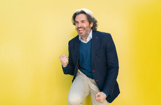 Happy businessman cheering while standing in front of yellow wall