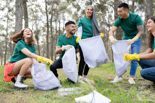 Young environmentalist friends collecting garbage in plastic bag at forest