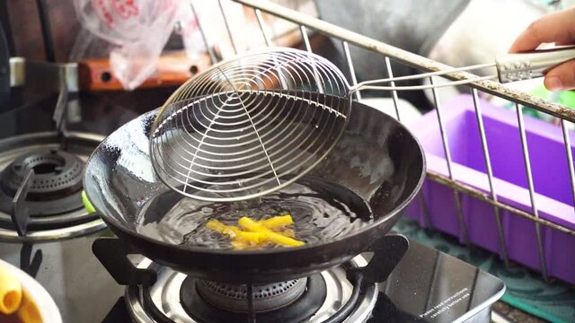 slow motion shot of fryum far far starchy bobby potato starch snack being put into boiling oil in a deep fryer where it expands puffs of steam come out and it's picked up with a sieve with the oil