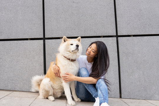 Mid adult woman sitting with Akita dog by wall