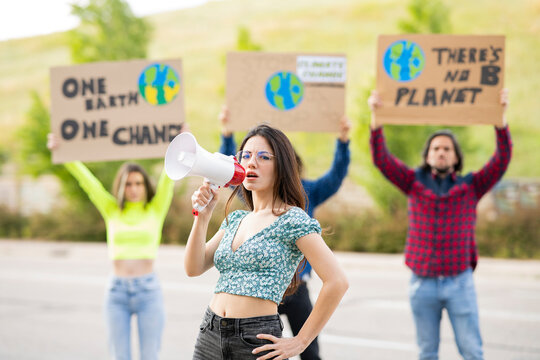 Female activist with hand on hip holding megaphone on footpath