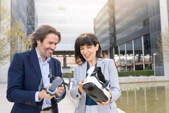 Smiling male and female professionals holding drone and virtual reality headset in park