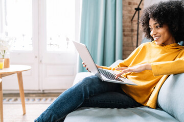 Young woman using laptop while sitting on sofa at home