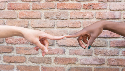 Women touching index fingers by brick wall